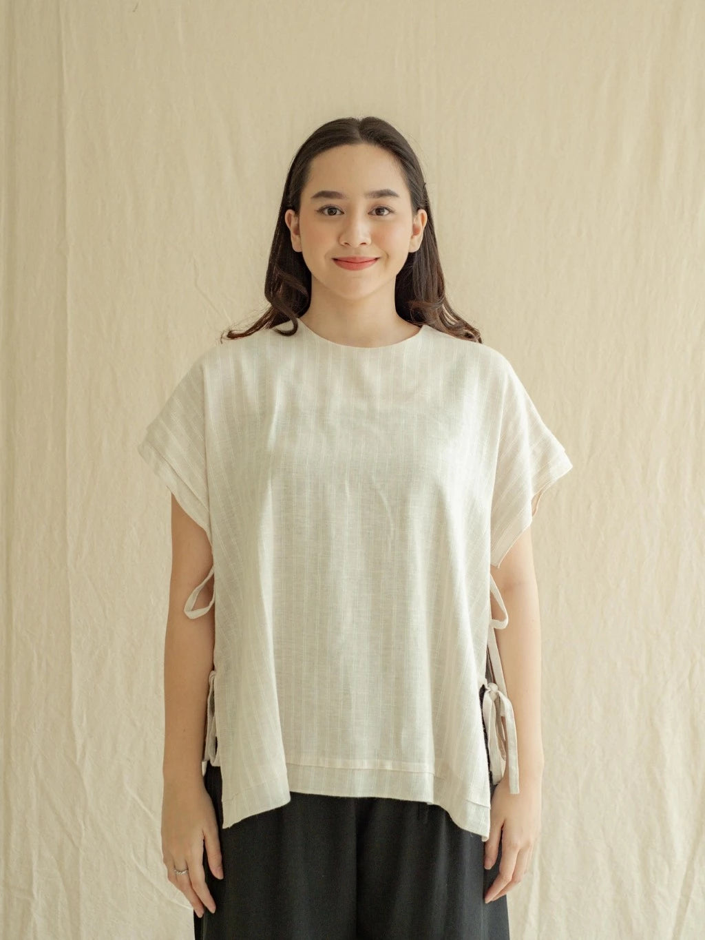Woman wearing Vest Samara, a light-colored top with cut-out sleeves from Labuan Linen Wear, against a beige background