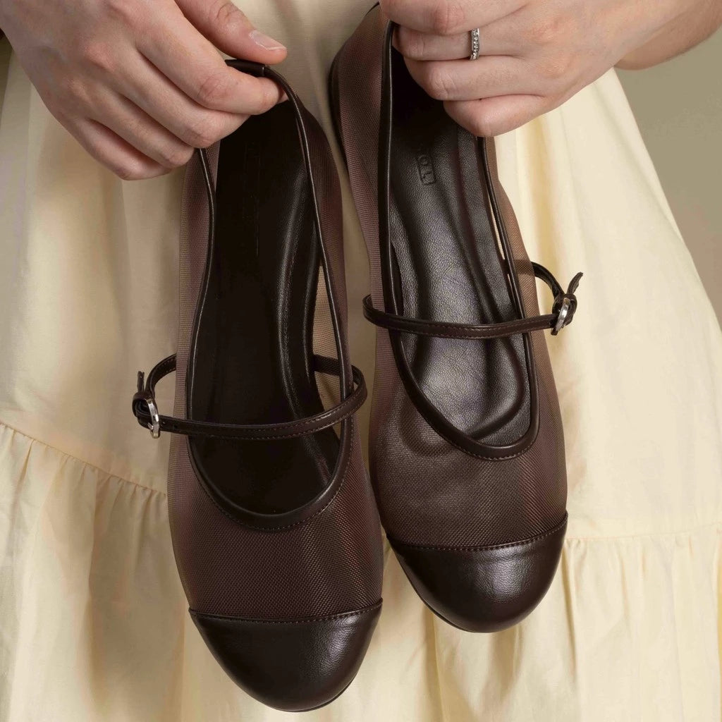 Brown transparent flat shoes with a strap held by hands against a beige background