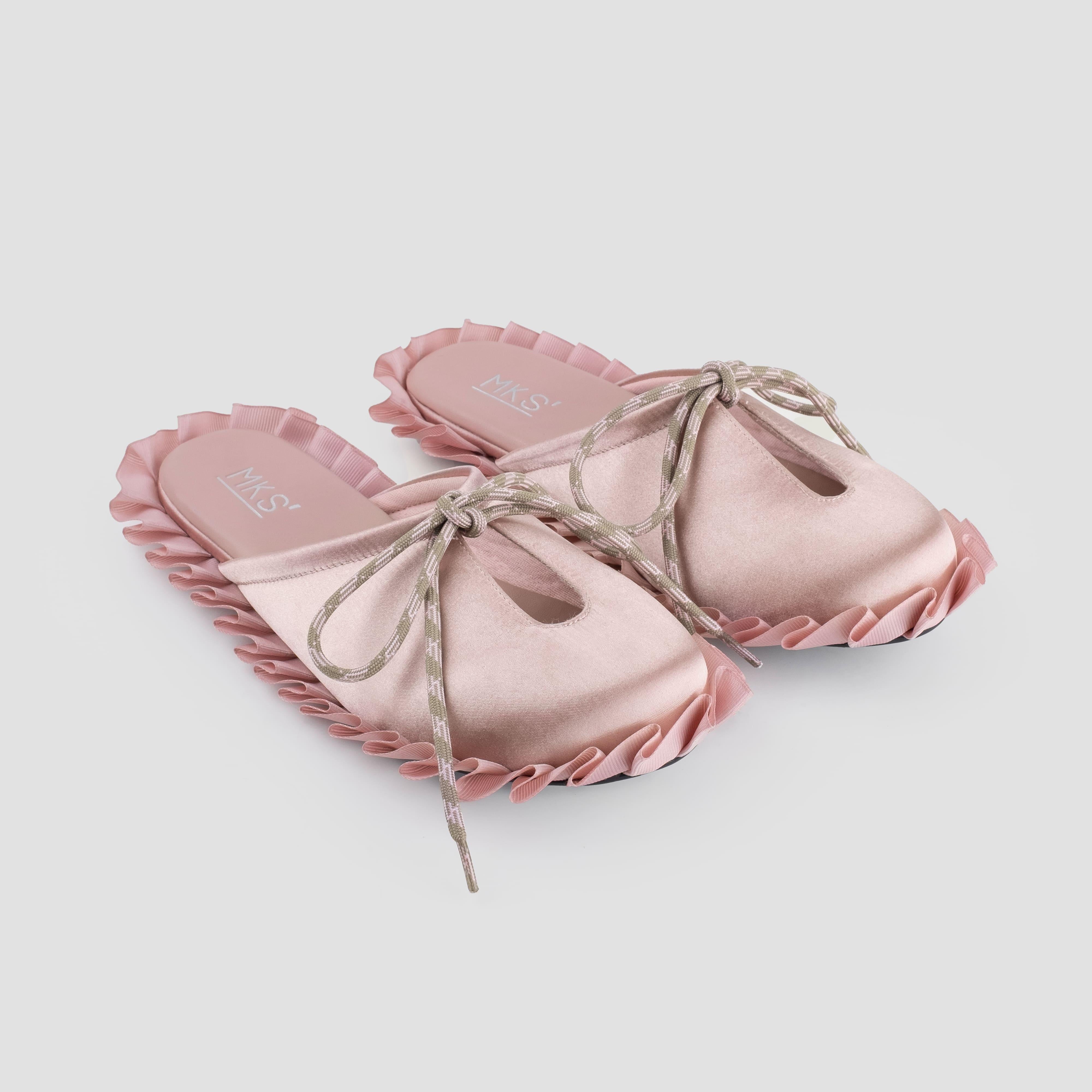 Pair of pink sandals with ruffled edges and a bow by MKS shoes on a light gray background