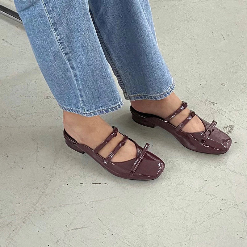 Brown strappy flat shoes worn with light blue jeans on a light gray floor.