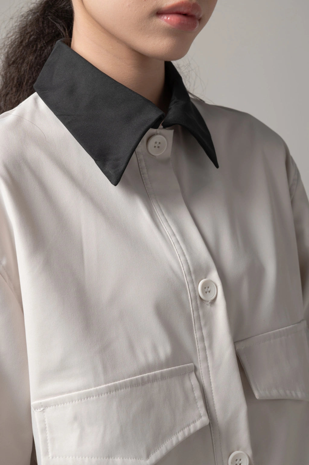 Close-up of a person wearing a broken white trucker jacket with a black collar by Kajuaruna against a neutral background