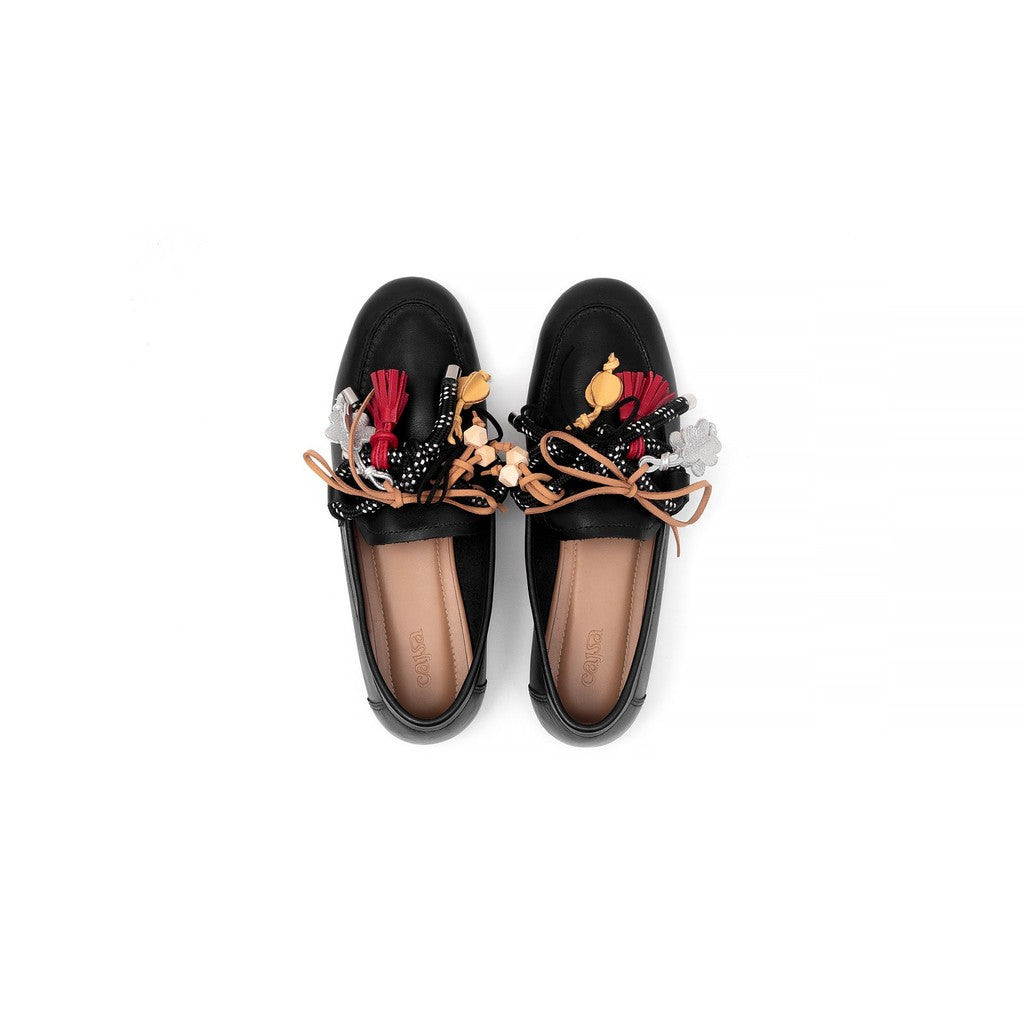 Black loafers flatshoes with colorful floral and bow embellishments on a white background