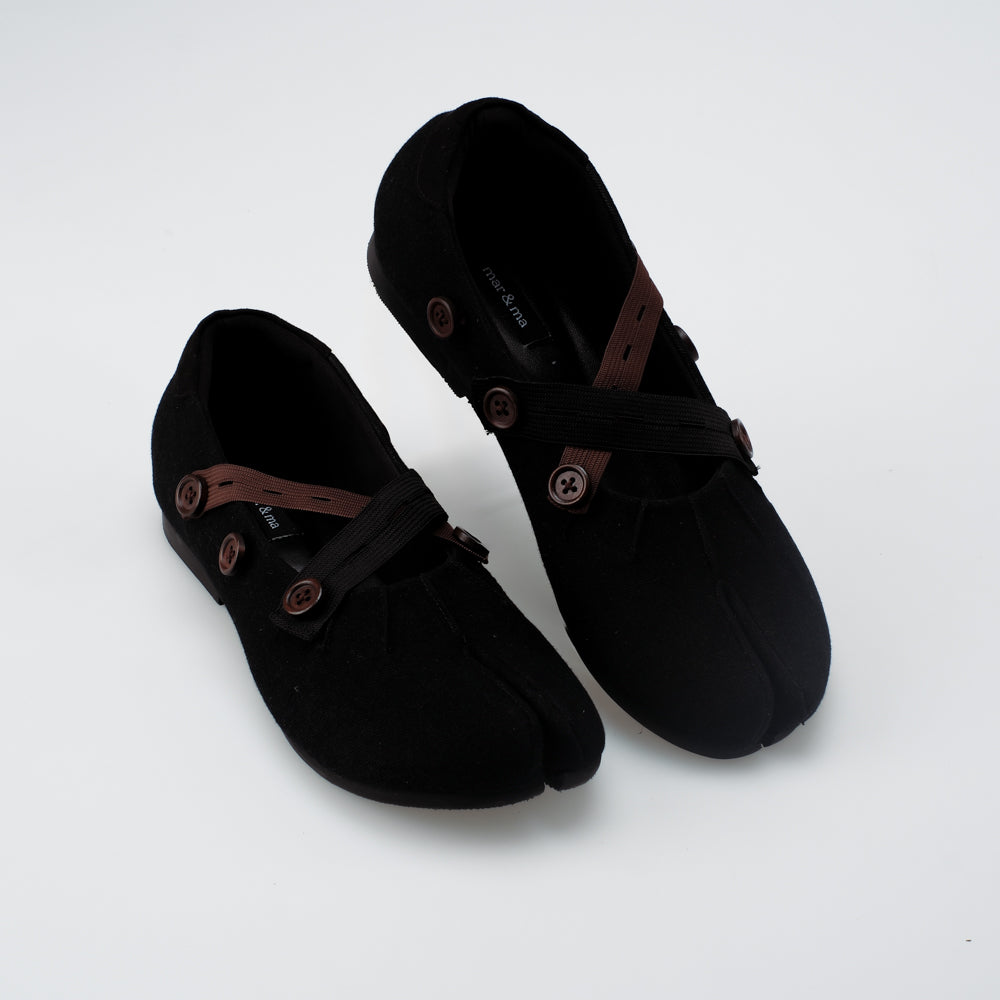 Pair of black flat shoes with brown and black straps on a white background