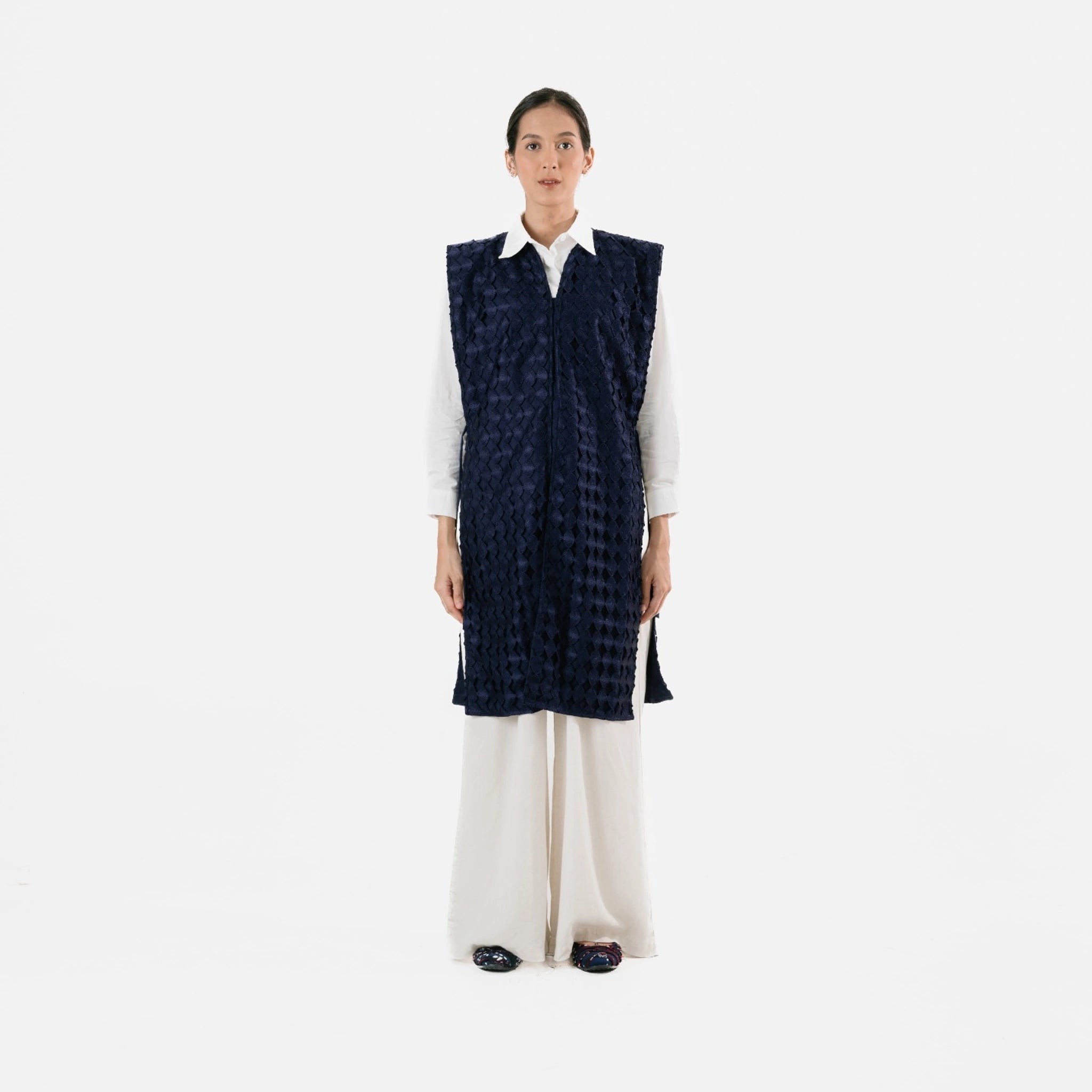 Person wearing a navy checkered long vest by Damakara over a white shirt on a white background