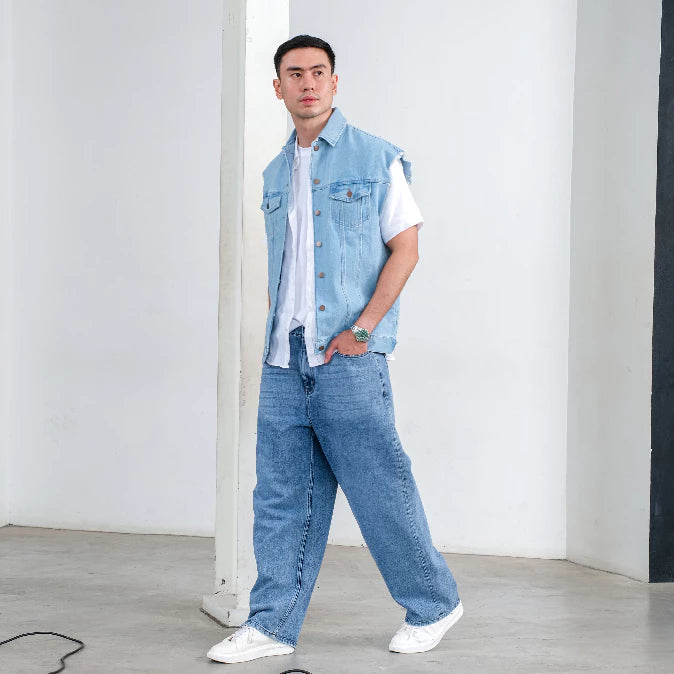 Man wearing Alexa Vest Denim, a sleeveless button-up denim vest with front flap pockets and raw-cut armholes from Ambra La Moda, paired with white shirt and white sneakers in a minimalistic setting.