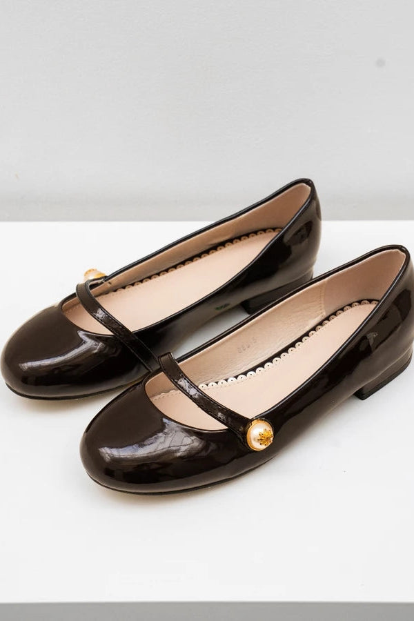 Pair of black patent leather flat shoes with a gold button on a white background