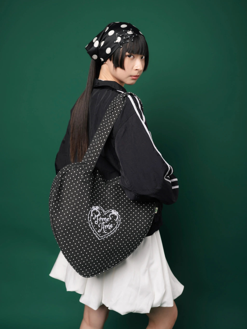 Person wearing a black polka dot bag with a heart design from Tome Ame on a green background