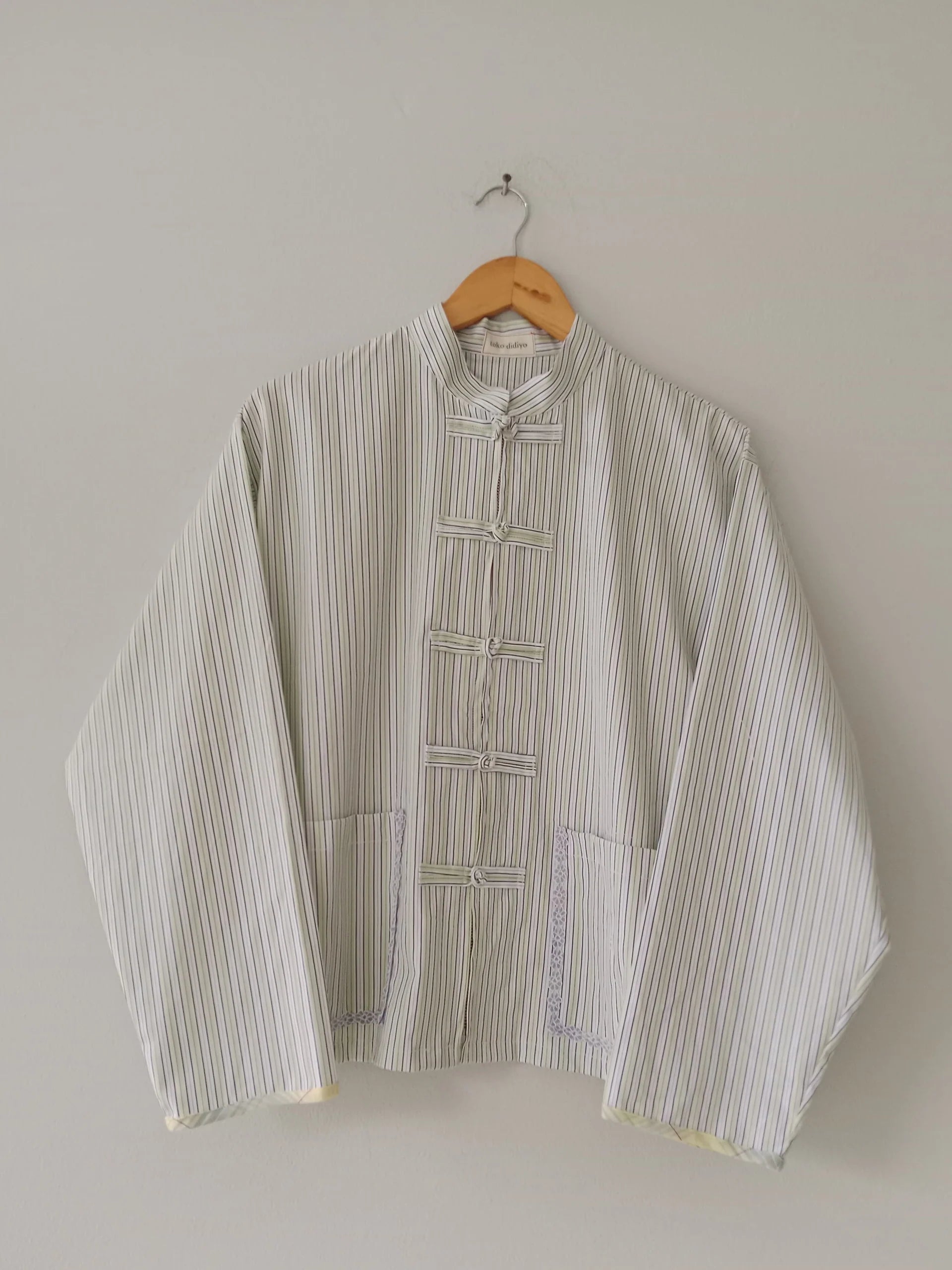 Striped cheongsam shirt by Toko Didiyo on a hanger against a plain background