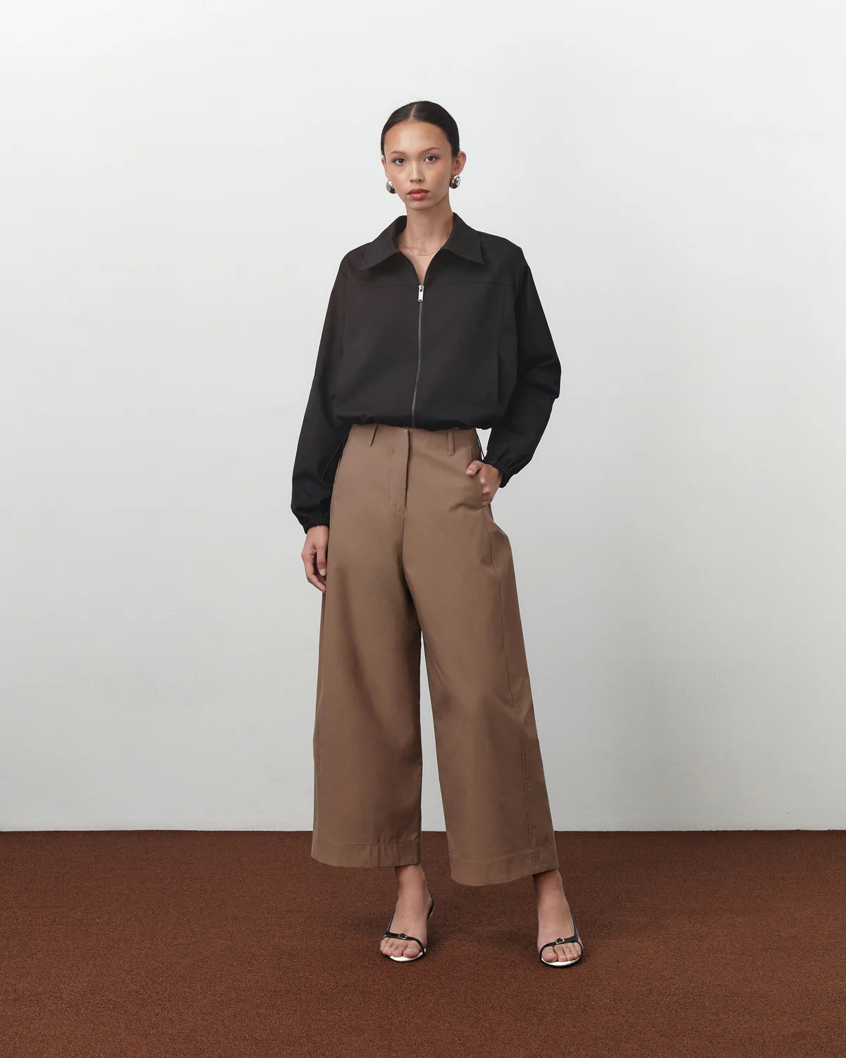 Person wearing a black Anders Jacket by Acheté de Nous and brown pants on a white background