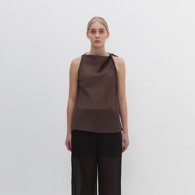 Woman wearing a brown sleeveless blouse by Morningsol and black pants on a white background