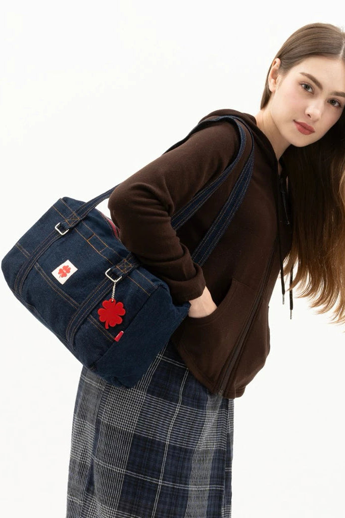 Woman holding a dark blue denim shoulder bag by Luella with a red floral emblem on a white background