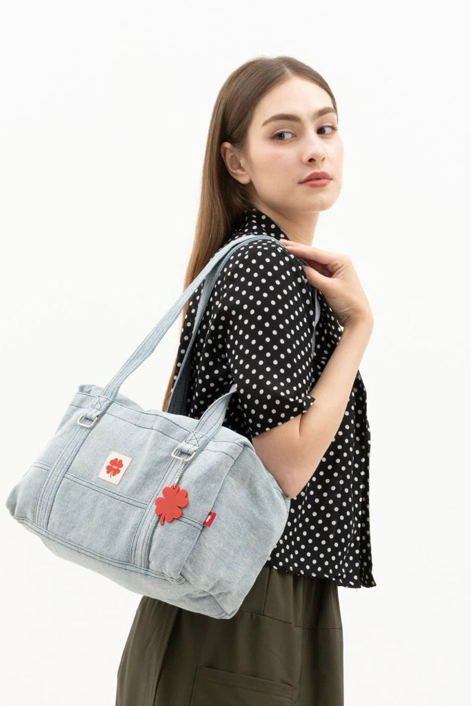 Woman holding a light blue denim shoulder bag by Luella with floral details on a white background