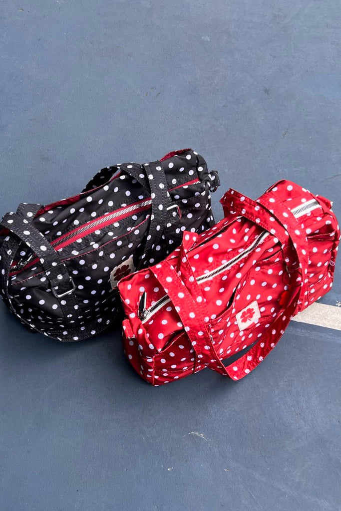 Two polka dot bags by Luella, one black and white, one red and white, on a gray surface.