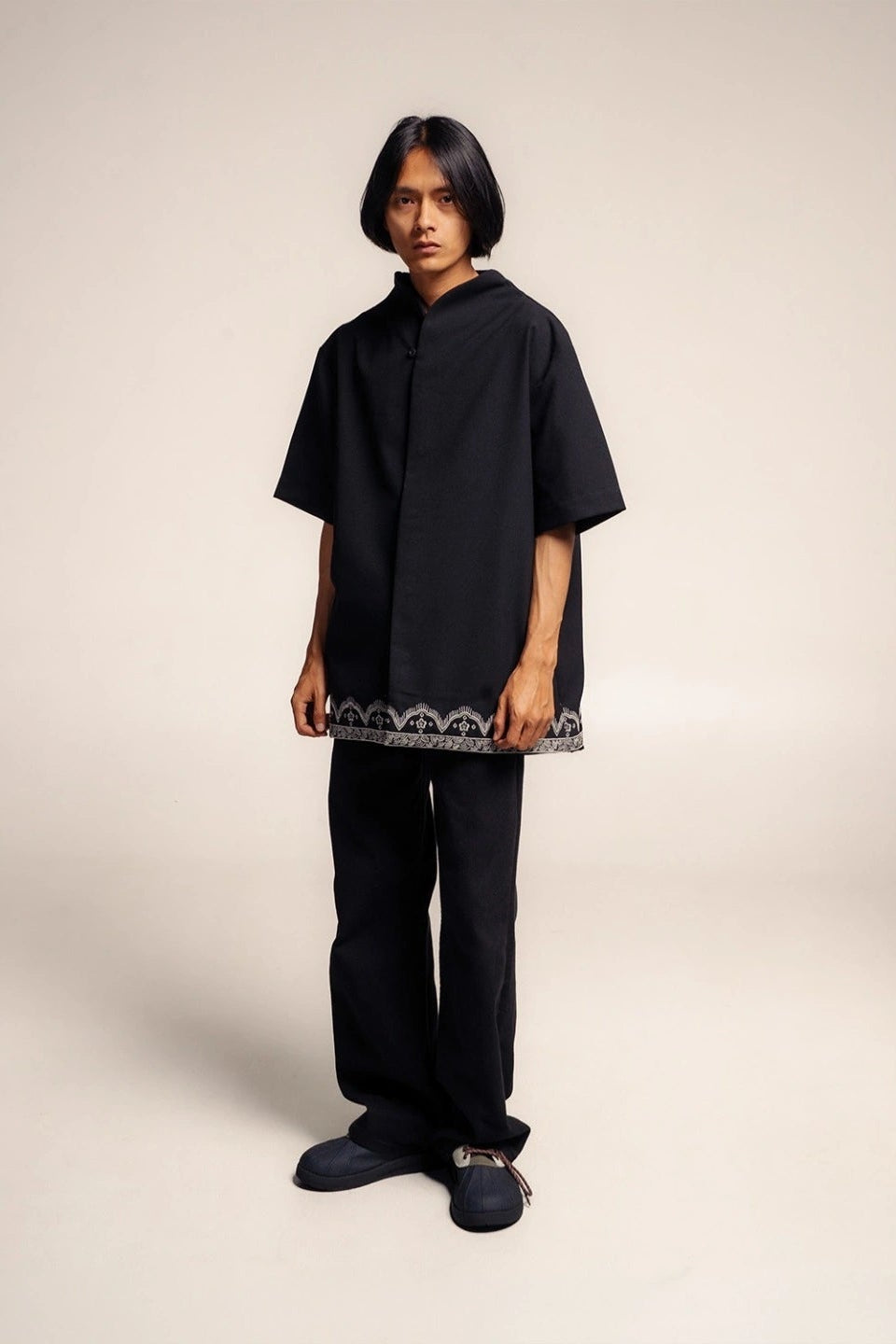 Person wearing a black shirt with a patterned hem by Damakara on a beige background