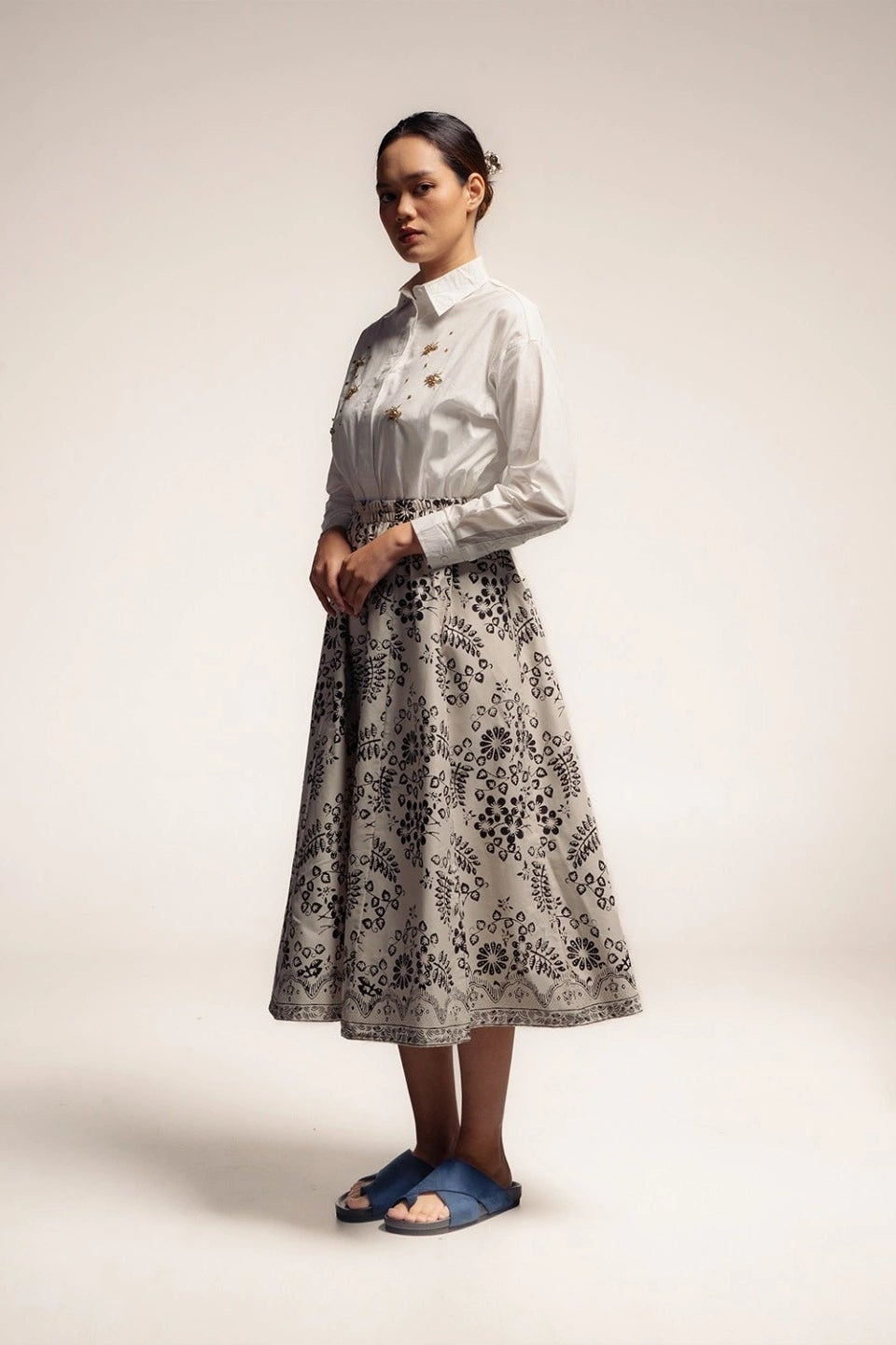 Woman wearing a white blouse and black floral skirt by Damakara on a plain background