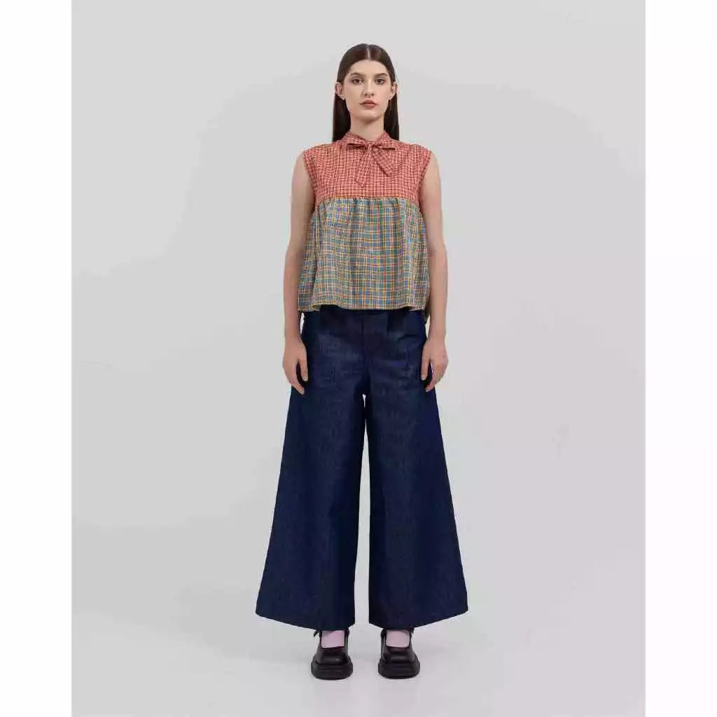 Woman wearing a sleeveless checkered top by Tuff Puff and wide-leg jeans on a white background