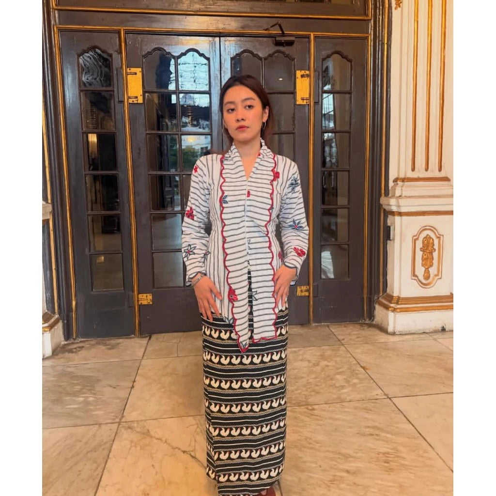 Woman in a patterned dress and black patterned saroong by Merona standing in front of a decorative door.