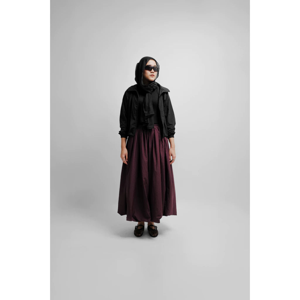 Woman wearing a flowy dark red maxi balloon skirt styled with a black top and outerwear.