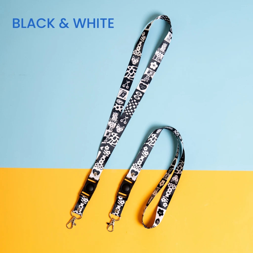 A black and white lanyard strap with a variety of patterns including hearts and bones, displayed against a yellow and blue background.