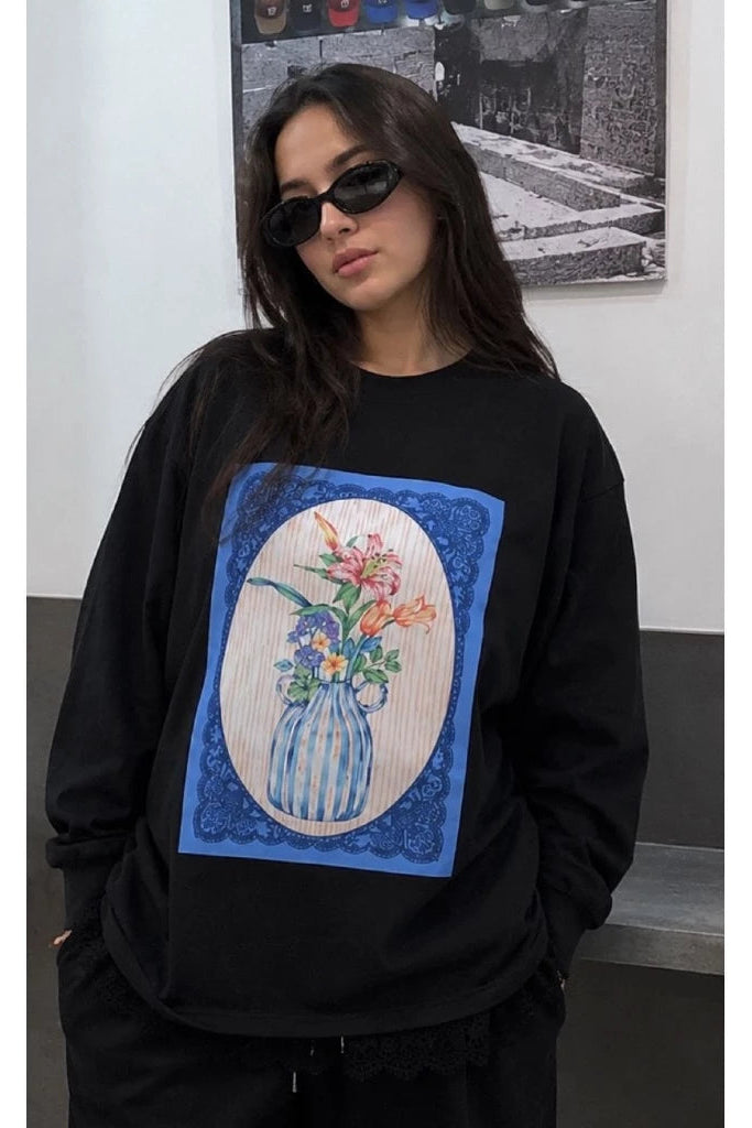 Person wearing a black sweatshirt with a floral design in an oval frame by Tuff Puff.
