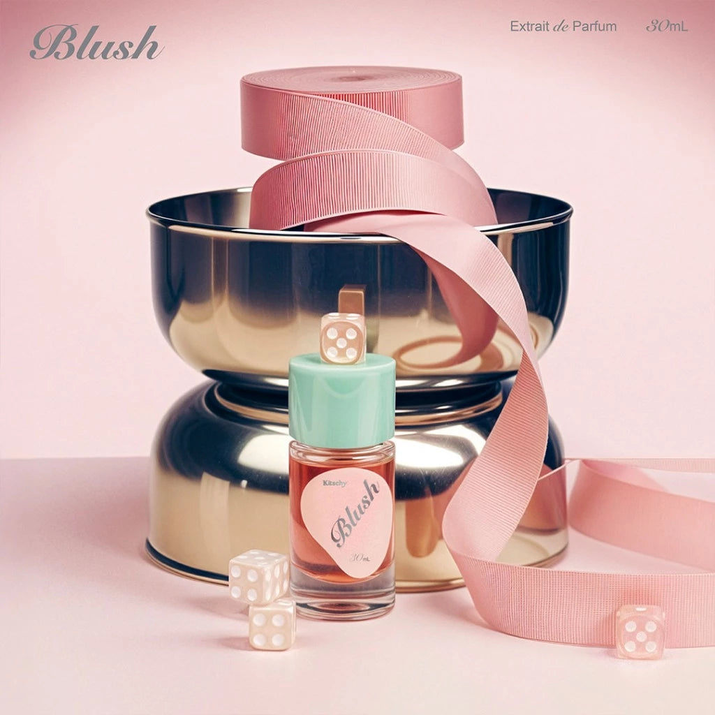 Perfume bottle labeled 'Blush' from Kitschy with a pink ribbon and dice on a pink background