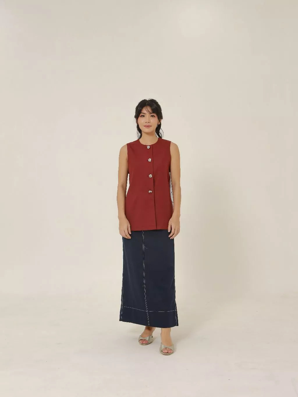 Woman wearing a red sleeveless vest and dark blue skirt on a beige background