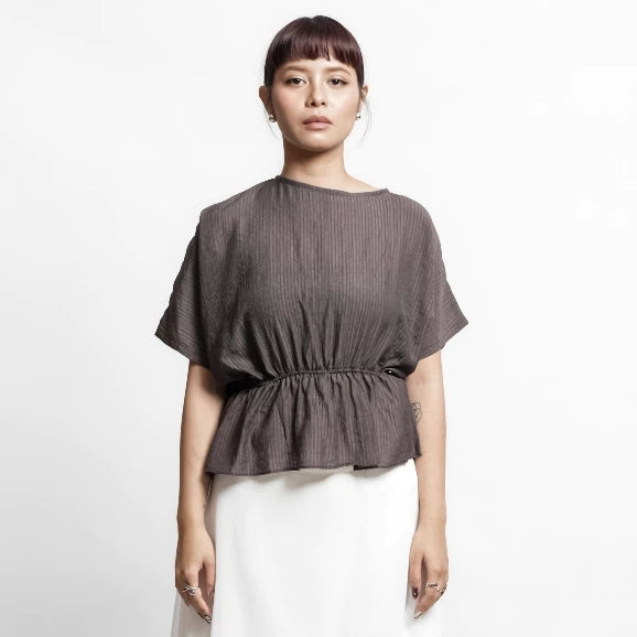 Woman wearing a brown textured top by Isoos Studios and white skirt on a white background