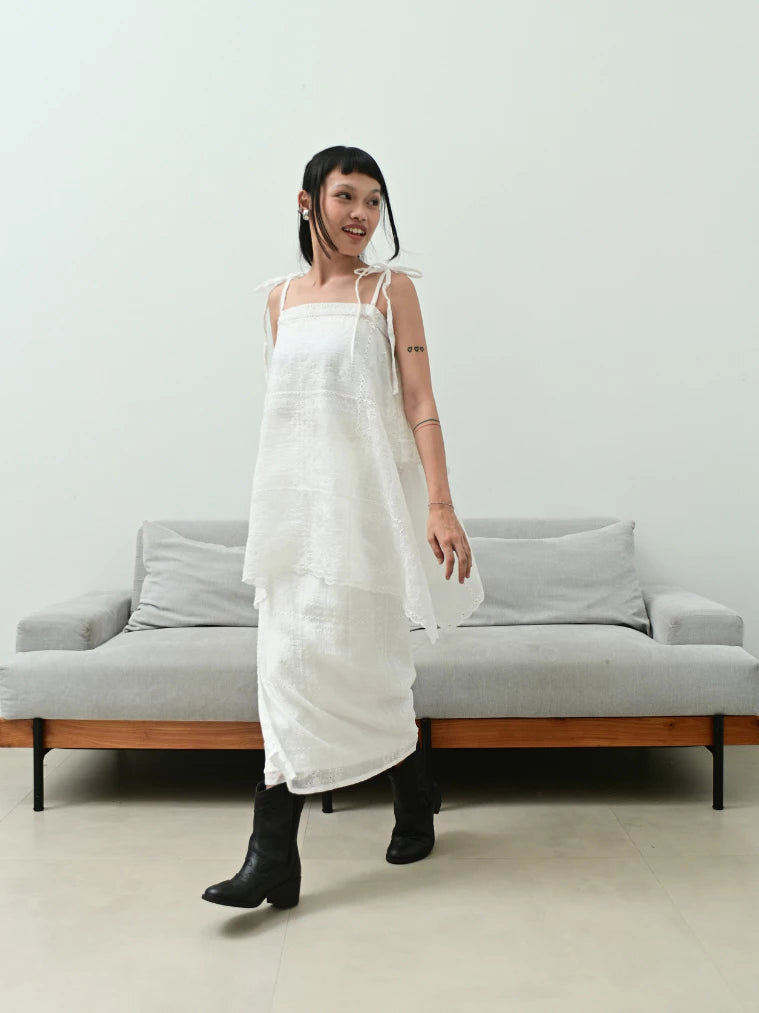 Woman wearing a white sleeveless top by Tuff Puff standing in a minimalistic room with a gray sofa.