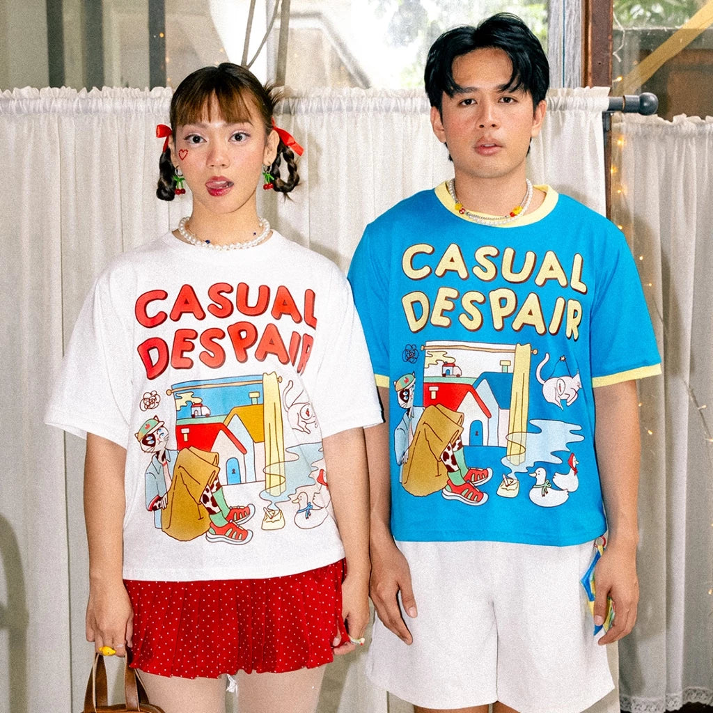 Two people wearing 'Casual Despair' t-shirts by Oh.Irv with colorful graphics in front of a white curtain.