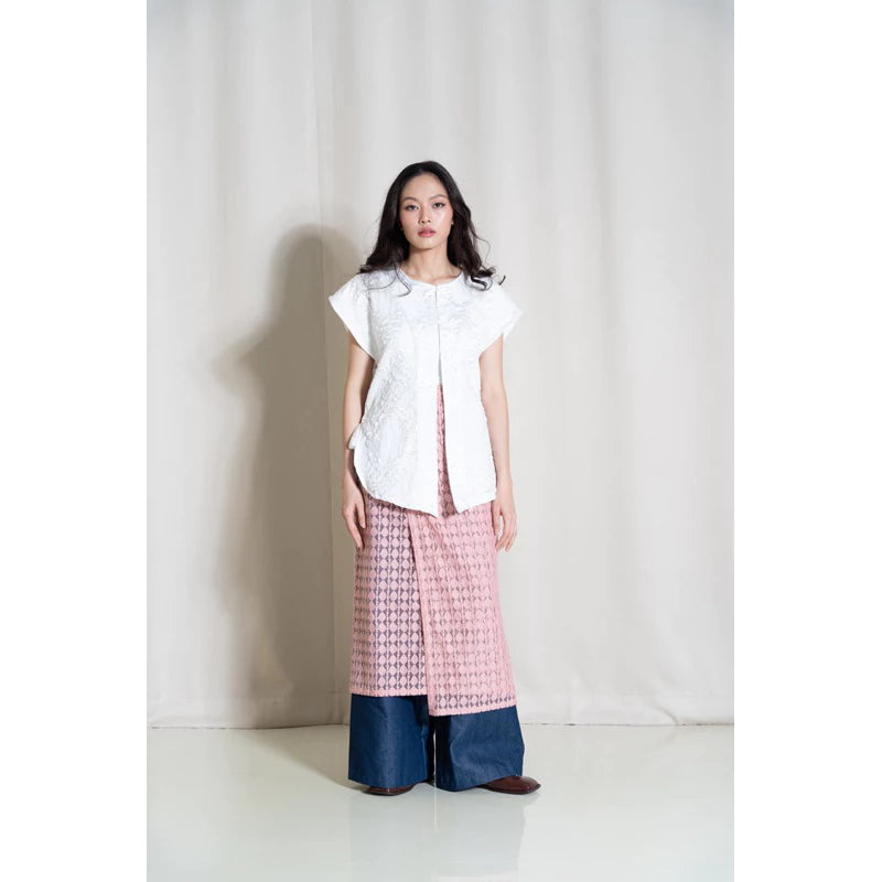 A person standing in a studio setting, wearing a white top and the Cemara Lace Skirt in pink. The skirt is long and has a floral pattern.