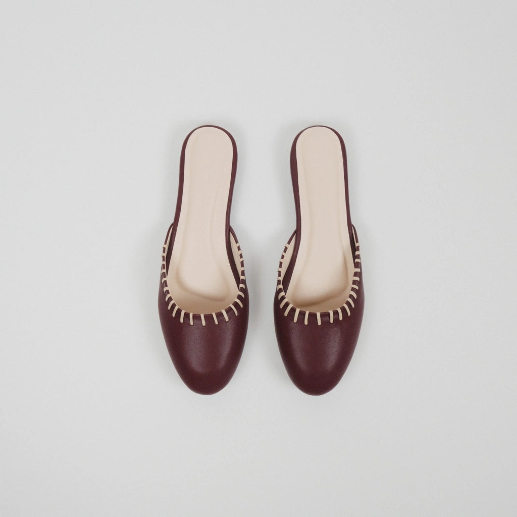 Pair of Amara Sol dark red flatshoes with beige trim on a light gray background
