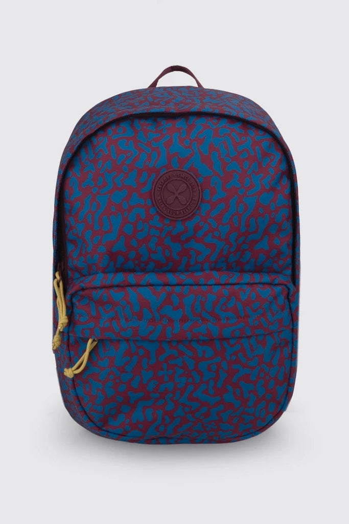 A Kaviar backpack by Exsport Bag in a blue and burgundy abstract pattern, featuring a circular embossed logo patch on the front pocket and gold-toned zipper pulls, set against a light gray background.