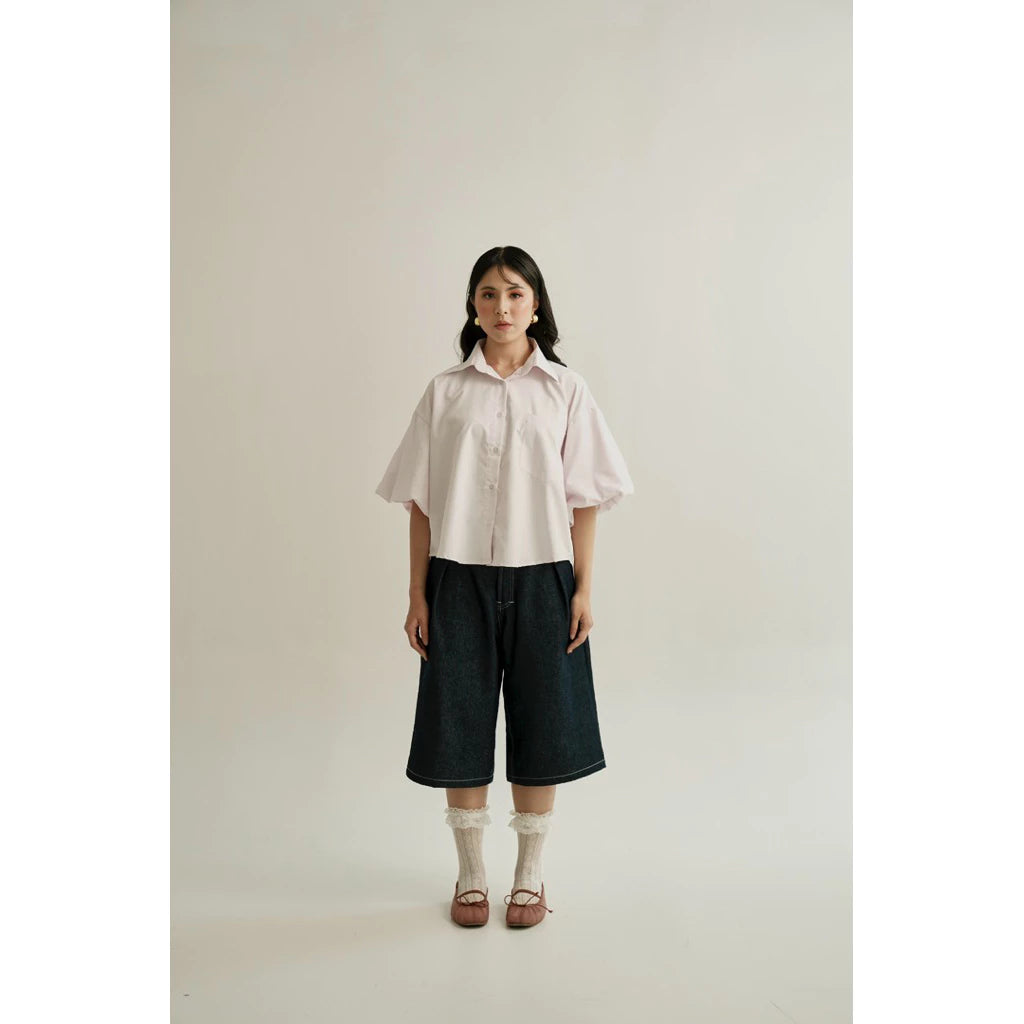 Person wearing a light pink shirt and dark jorts pants on a plain background