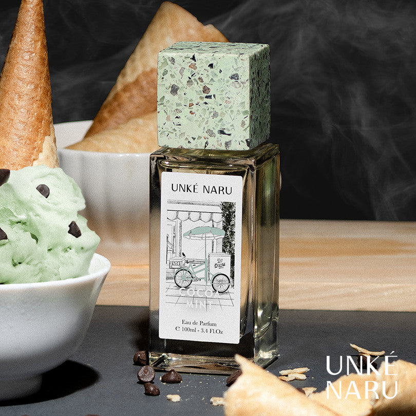 A bottle of 'Cocoa Mint' perfume by Unke Naru with a green cap, placed next to a bowl of mint ice cream and a hazelnut, in a stylized presentation.