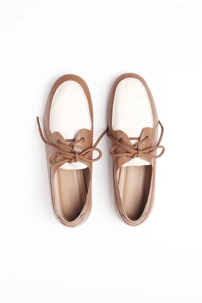 A pair of women's boat-style flatshoes by Cajsa in a light brown/tan leather with white toe caps, shown from a top-down view on a white background.