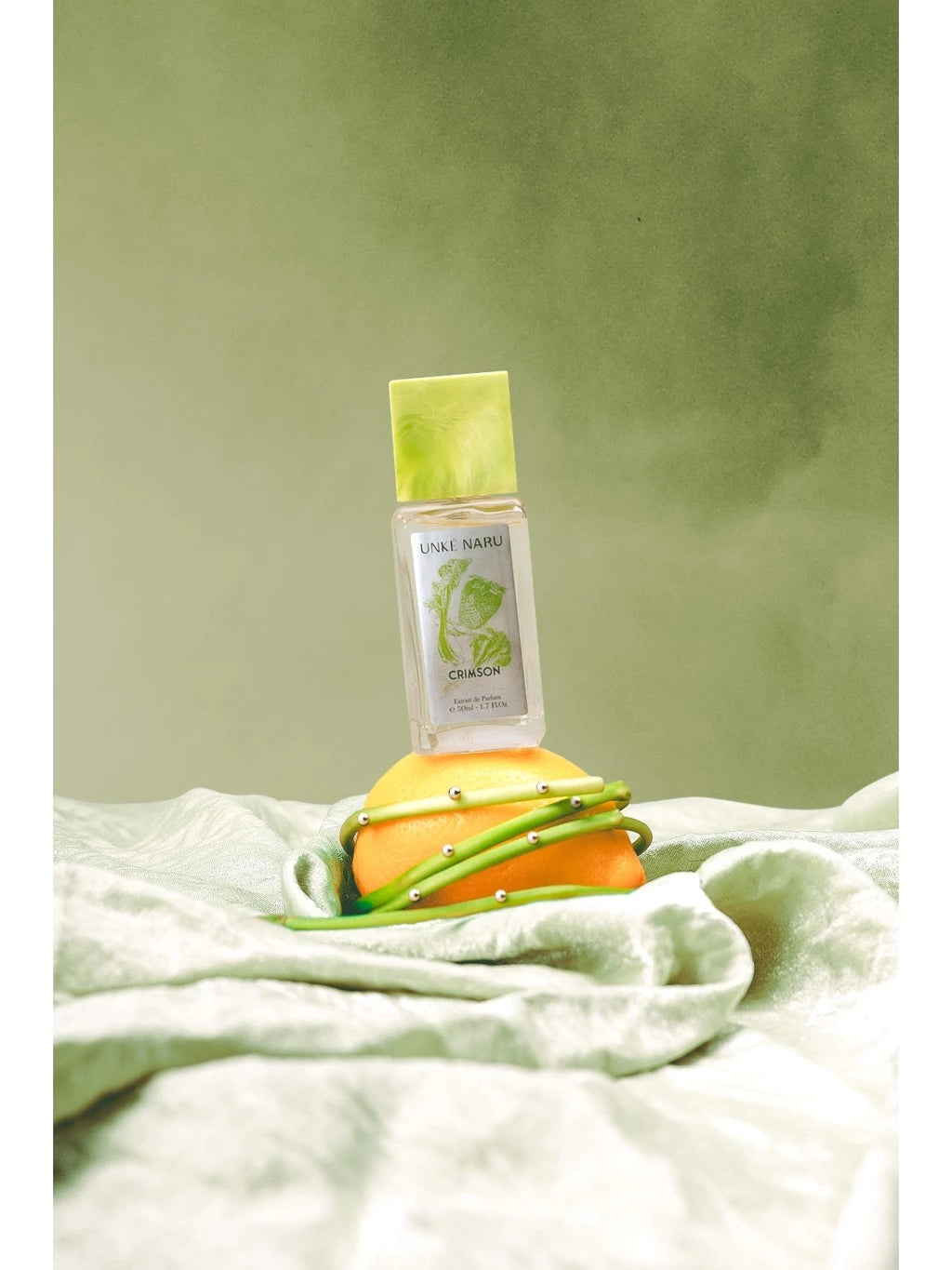 Crimson perfume bottle from Unke Naru with a green cap on an orange against a green background