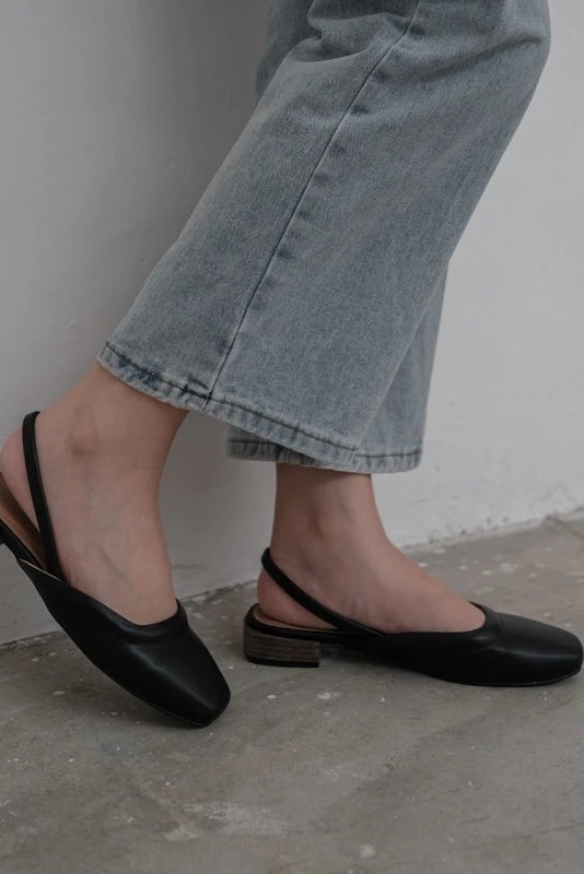 Person wearing black flatshoes by Tangerine Marche and light blue jeans against a plain background