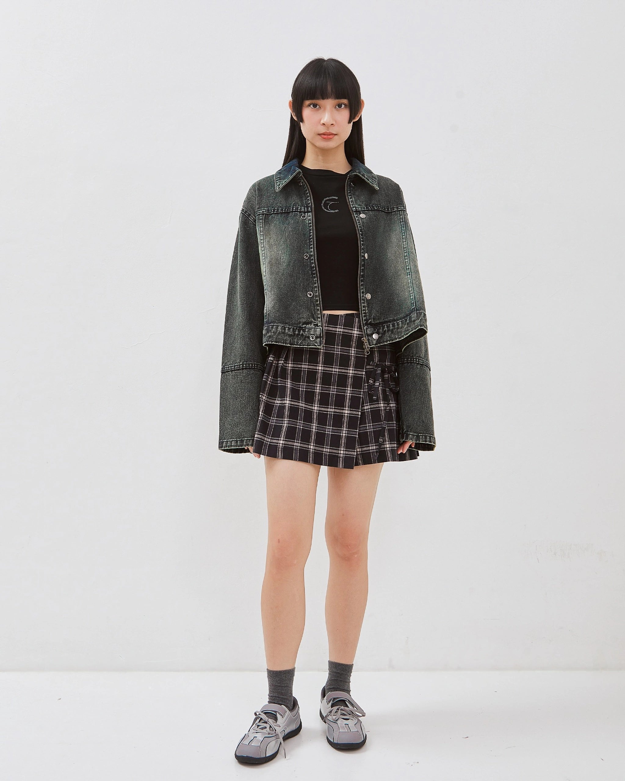 Person wearing a denim jacket, black top, tartan mini skirt, and gray shoes on a white background