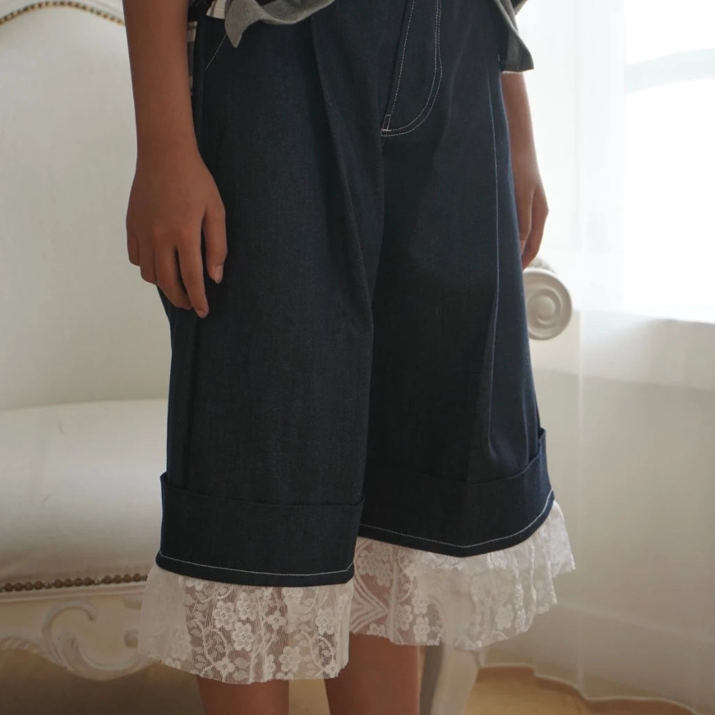 Person wearing dark denim jorts pants with lace trim in a softly lit room.