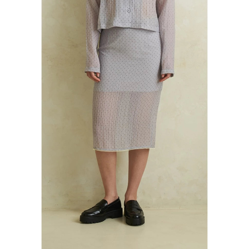 Person wearing a grey polka dot layered skirt with a plain background
