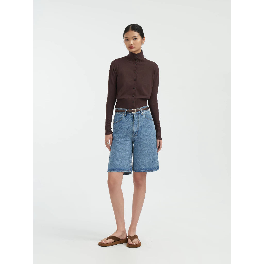 Woman wearing a brown turtleneck cardigan by Achete de Nous and blue denim skirt on a white background