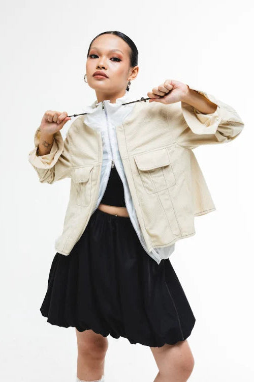 Person wearing a dual layer beige jacket by Wad Studio over a black top and skirt on a white background