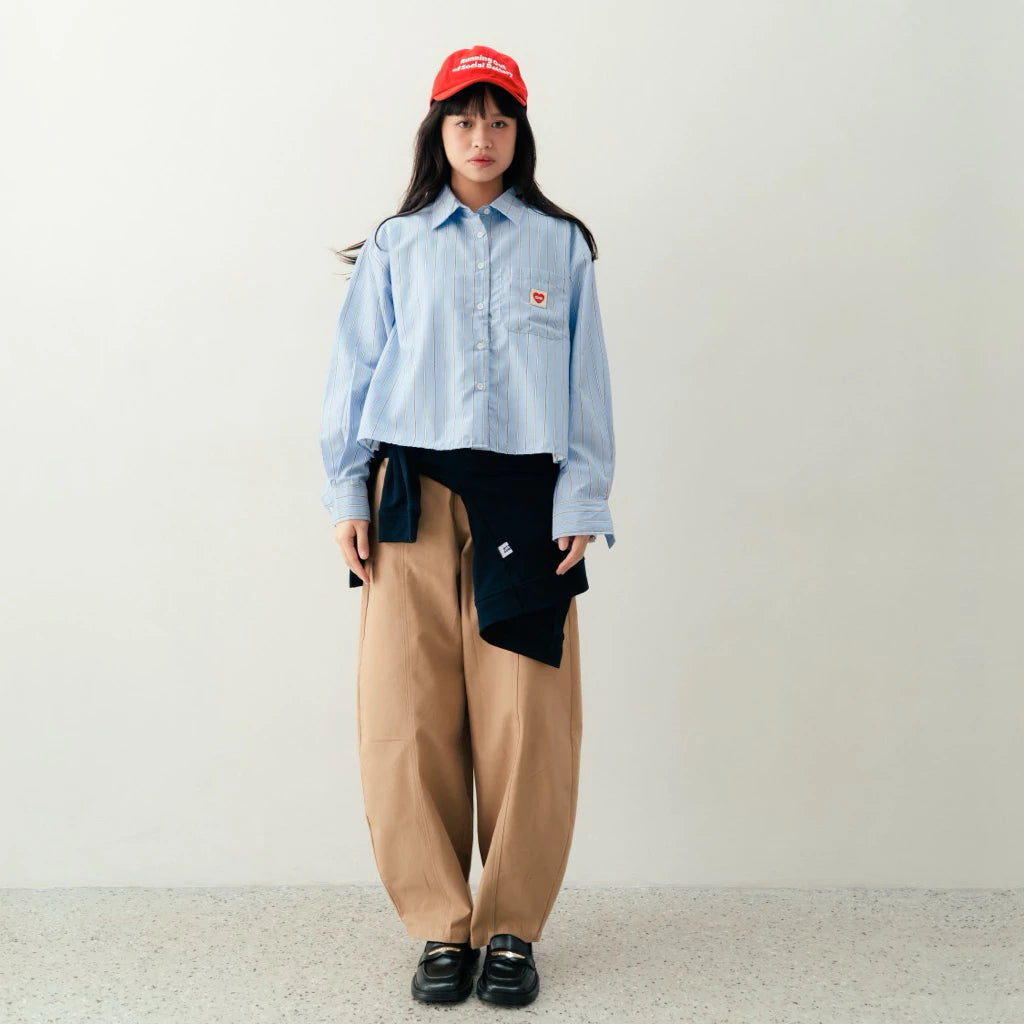 Person wearing a light blue stripped shirt by notyourcompany, beige pants, and a red cap on a plain background