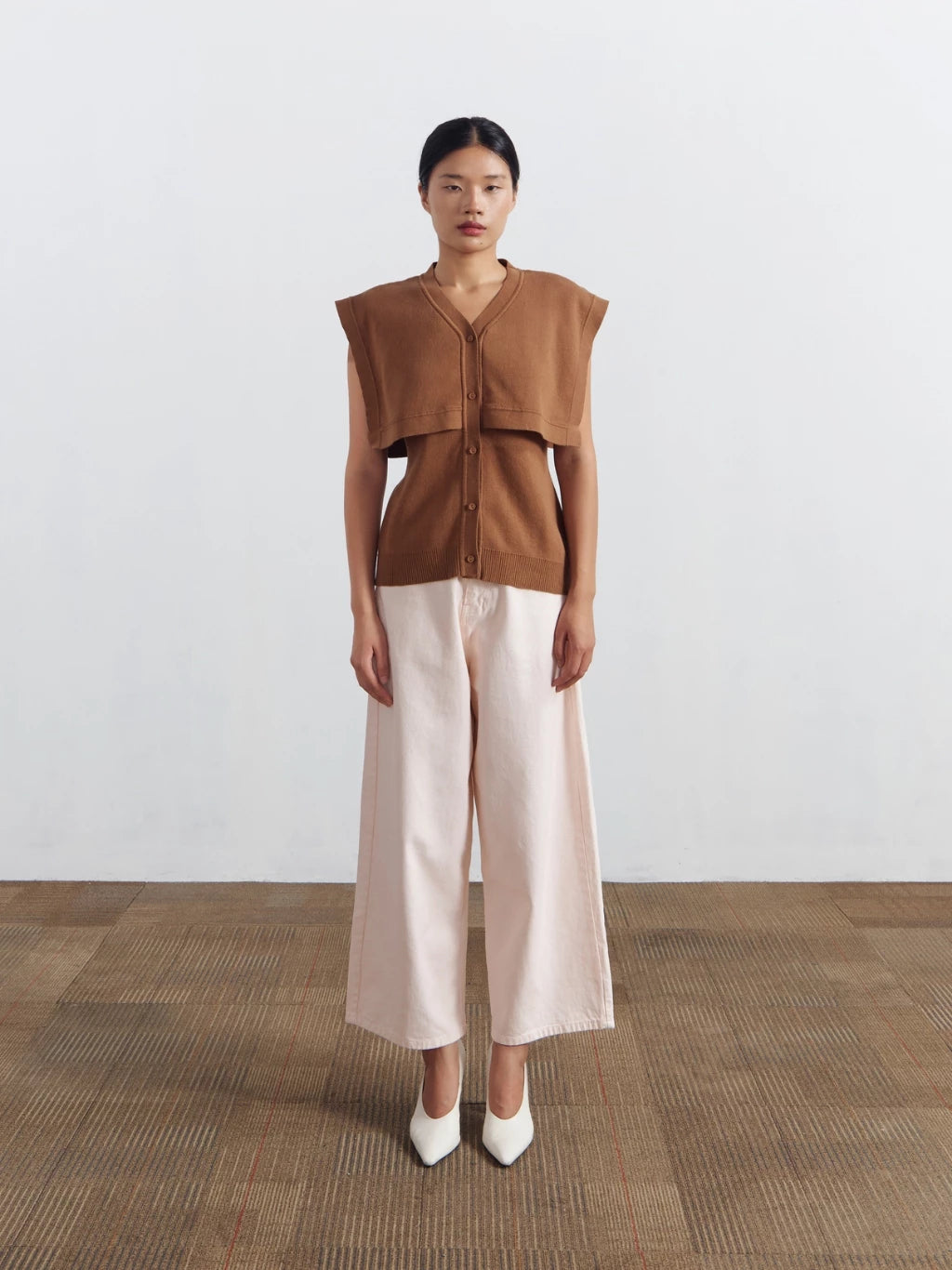 Woman wearing a brown sleeveless vest by Achete de Nous and beige pants on a white background