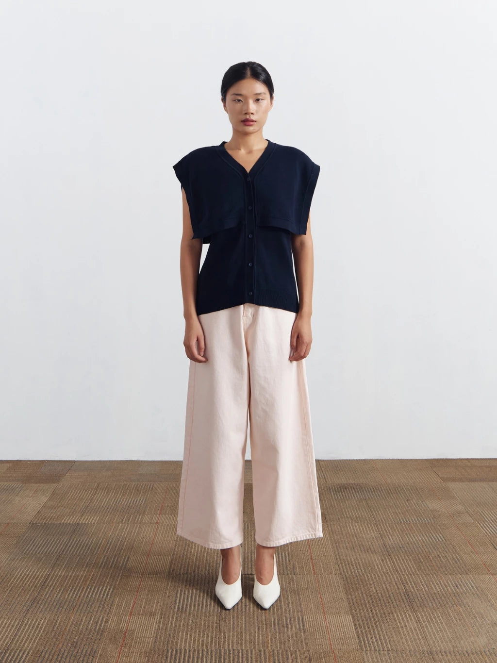 Woman wearing a dark blue sleeveless vest by Achete de Nous and beige wide-leg pants on a white background
