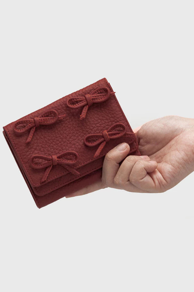 Hand holding a red textured wallet by Adorable Projects with bow details on a light gray background