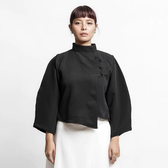 Person wearing a black traditional-style top by Isoos Studios with white skirt on a white background