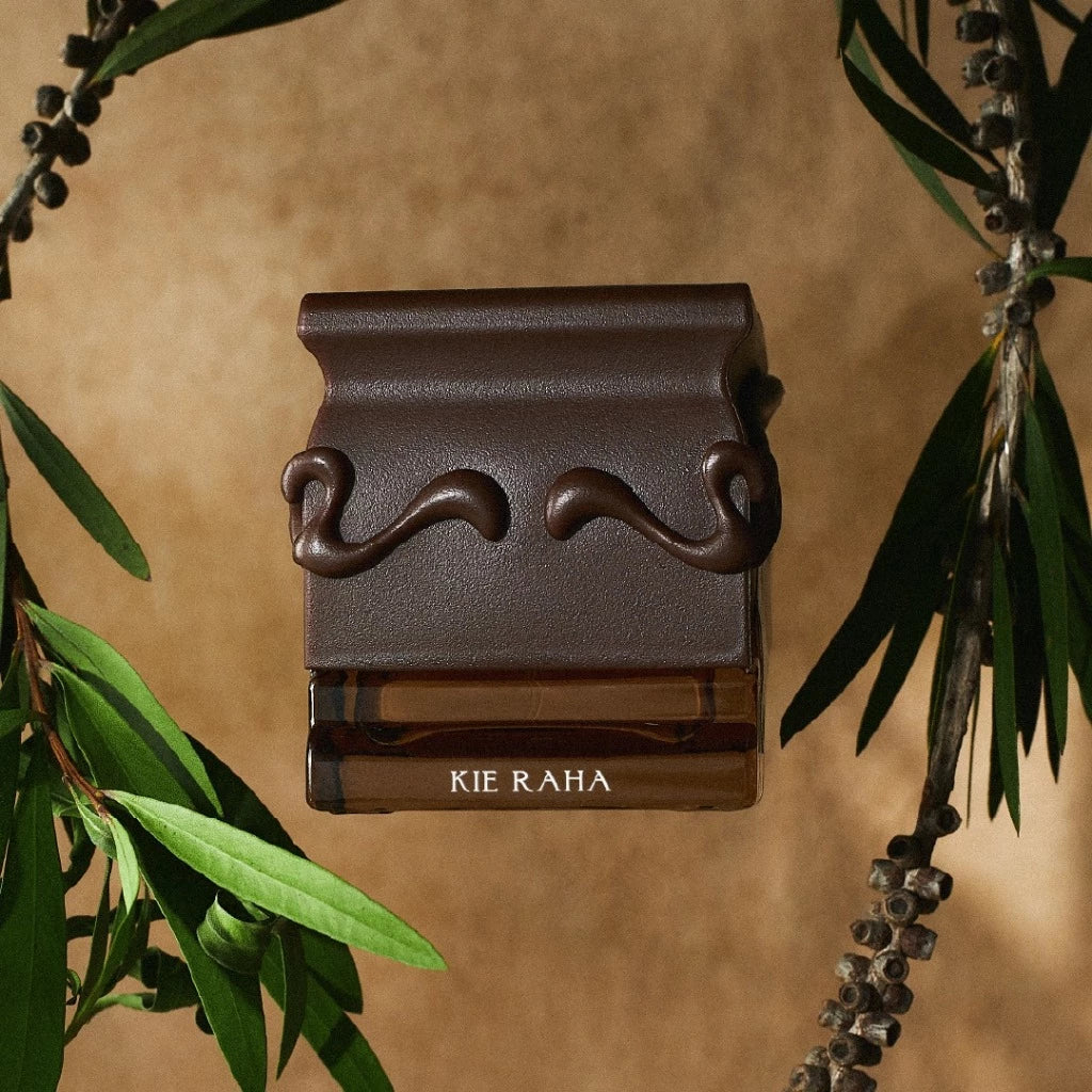 Kie Raha brown decorative perfume bottle from Saff & Co. on a beige background with green leaves.