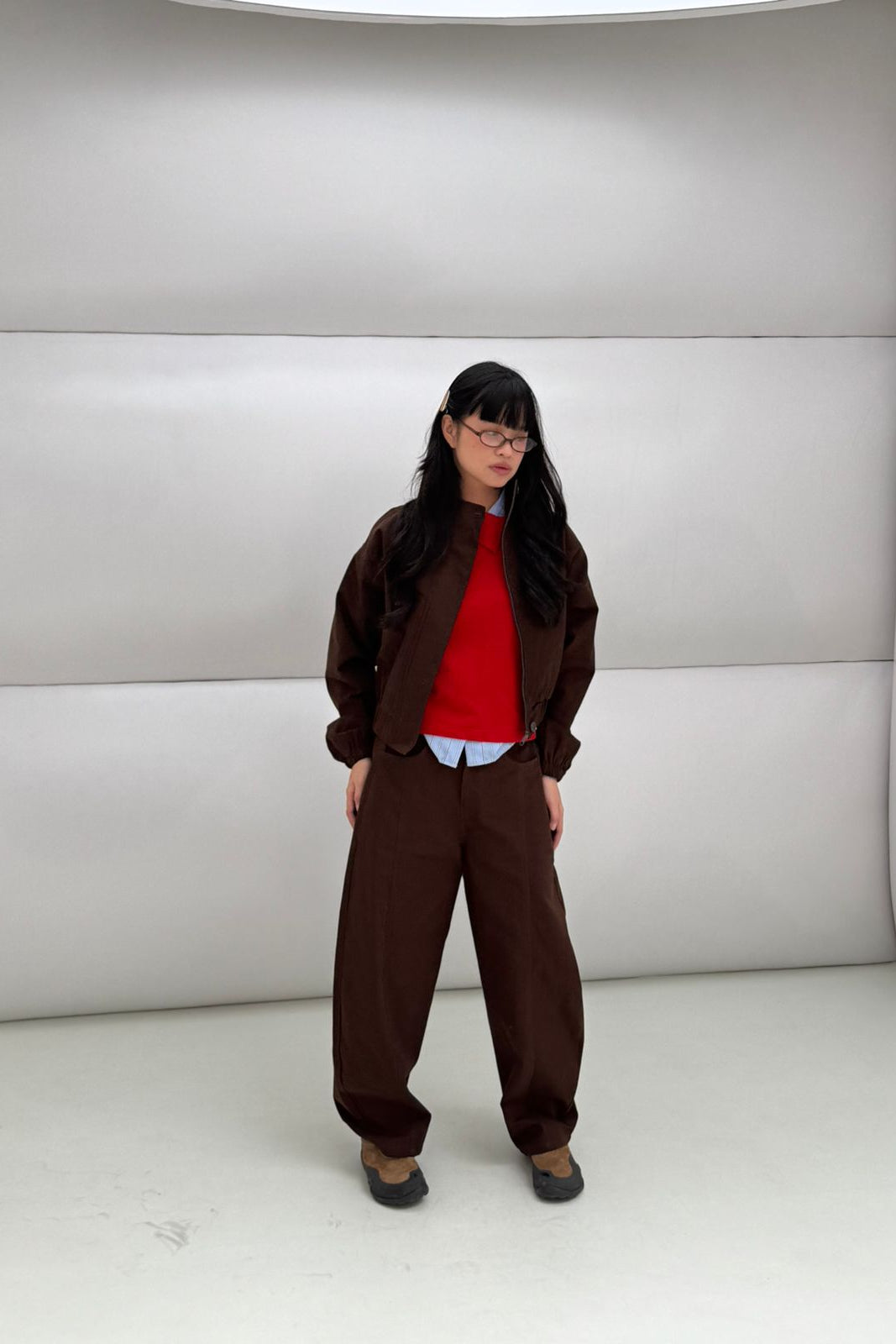 Person wearing a red shirt and brown jacket by notyourcompany with brown pants in a neutral setting