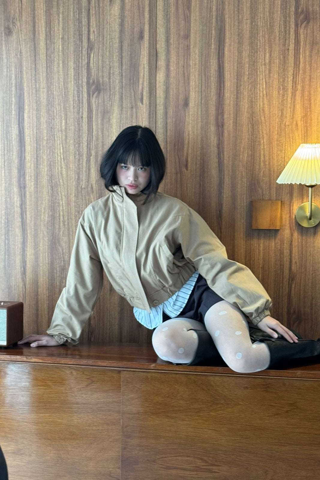 Person wearing cream jacket by notyourcompany, sitting on a wooden surface with a wooden wall background